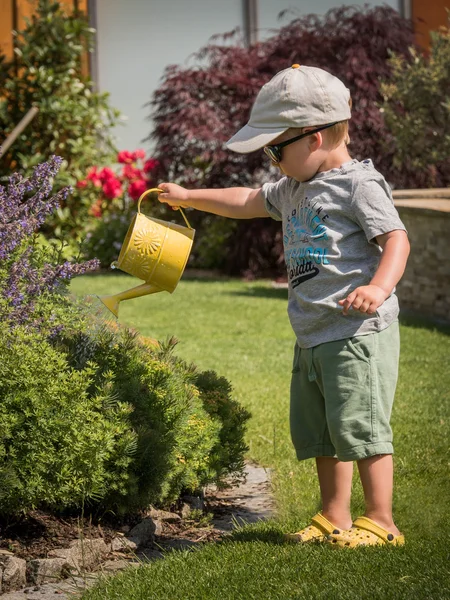 Niño pequeño con una lata de flores de riego en verano —  Fotos de Stock