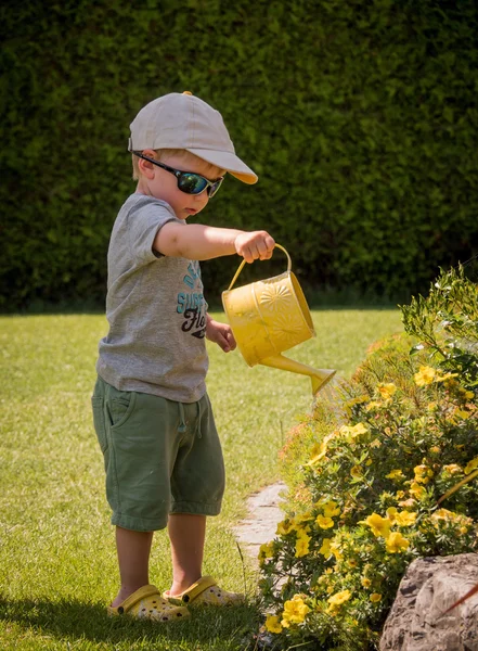 Little boy with a watering can watering flowers in summer — Stock Photo, Image