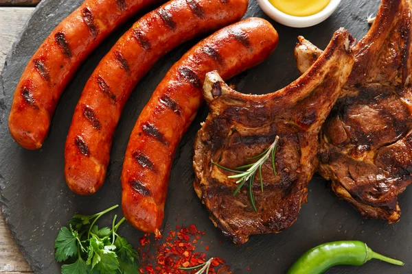 Saucisses grillées et steak sur le barbecue osseux — Photo