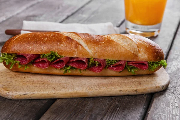 A szalámi és gyógynövények fafelületre baguette szendvics — Stock Fotó