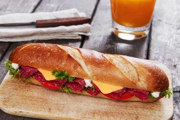 Sandwich à la baguette avec salami et herbes sur une surface en bois — Photo