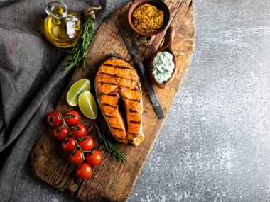 Izgara balık bifteği somon, ahşap bir tahtada alabalık, biberiye, domates, kapat.