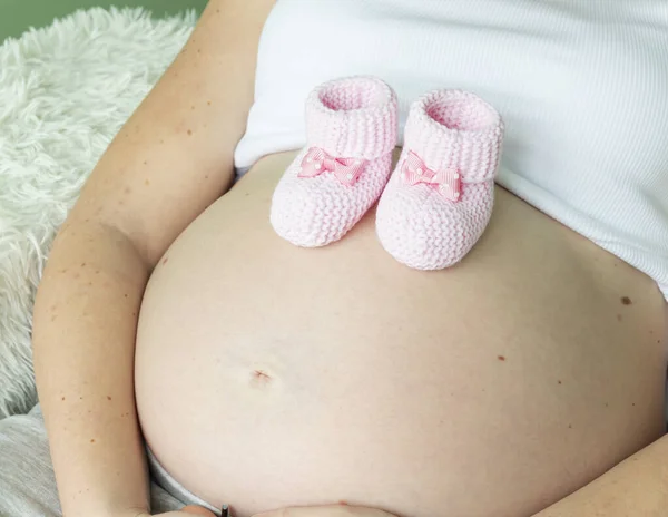 Nahaufnahme Einer Schwangeren Frau Mit Gestrickten Rosafarbenen Babybooties Auf Dem — Stockfoto