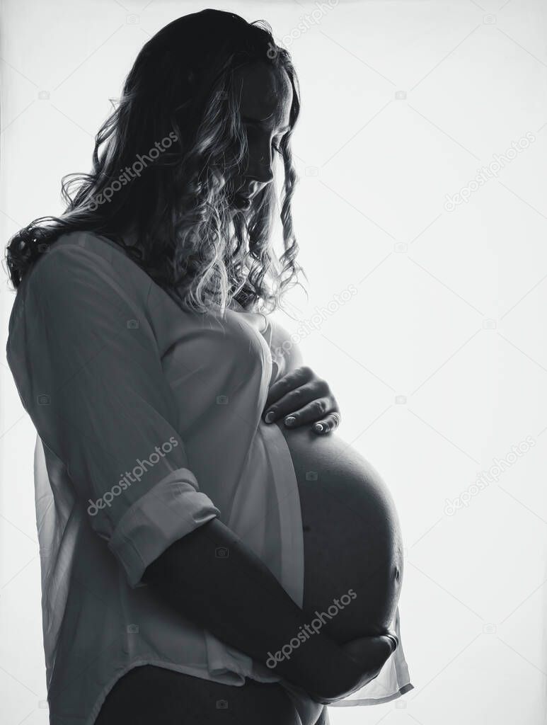 happy pregnant woman standing and clasping her belly with her hands black and white photography