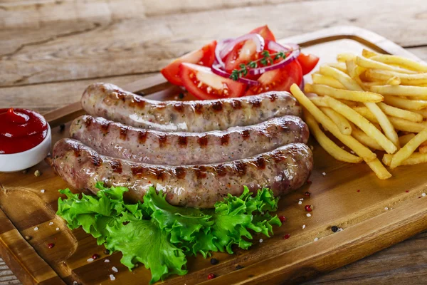 Grillwürste mit Pommes auf dem Schneidebrett — Stockfoto