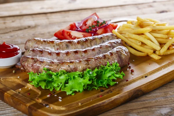 Grillwürste mit Pommes auf dem Schneidebrett — Stockfoto