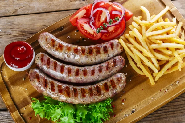 Salsichas grelhadas com batatas fritas em uma tábua de corte — Fotografia de Stock