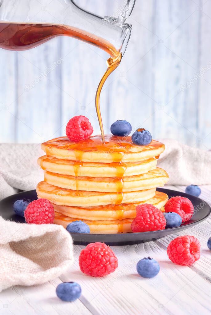 pancakes with fresh blueberries, raspberries are poured with maple syrup.