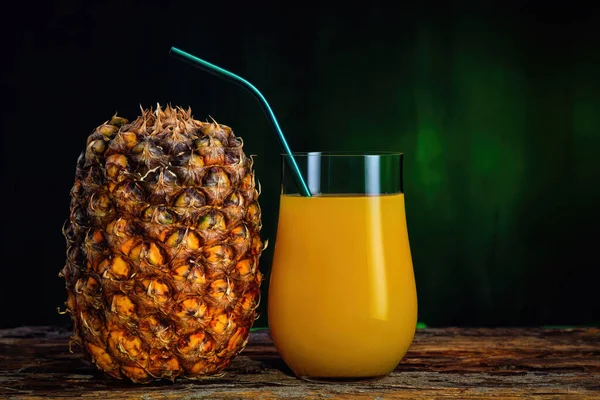 Succo d'ananas fresco in un bicchiere e ananas fresco su fondo verde scuro — Foto Stock