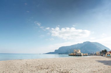 Turkuaz su, yumuşak kumlu kıyılar ve sakin kıyı şeridi boyunca uzanan küçük tarihi bir rıhtım inşaatı tarafından vurgulanan uzak dağlarla sakin bir sahil manzarası..