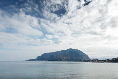 Uzak bir ada dağı, sakin bir su ve yumuşak bulutlarla dolu bir gökyüzü olan sakin bir sahil manzarası. Seyahat, doğa ya da huzurlu bir yaşam tarzı için mükemmel..