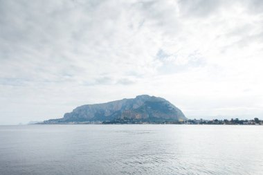 Uzak bir ada dağı, sakin bir su ve yumuşak bulutlarla dolu bir gökyüzü olan sakin bir sahil manzarası. Seyahat, doğa ya da huzurlu bir yaşam tarzı için mükemmel..