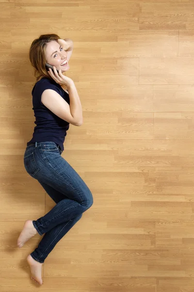 Smiling young woman with her mobile phone on the floor — Stock Photo, Image