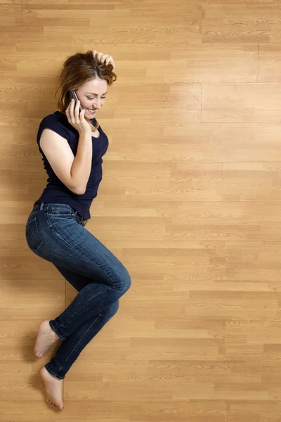 Lachende jonge vrouw met haar mobiele telefoon op de verdieping — Stockfoto