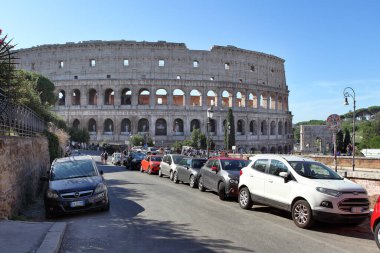 Roma, İtalya - 20 Eylül 2025: Güneşli bir günde Roma 'da kolezyum ön planda arabaların park edildiği, antik mimari ve modern yaşam arasındaki zıtlığı gösteren.