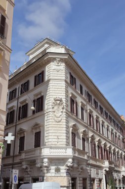Roma, İtalya - 17 Eylül 2025: Açık mavi gökyüzünün altında cephede süslü bir arma ile Barok Roma sarayı köşesi. Kahverengi kepenkler pencereleri vurguluyor.