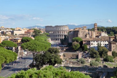 Roma, İtalya - 21 Eylül 2025: Roma 'daki Kolezyum ve Roma Forumu' na bakan manzara. Turistler Via dei Fori Imperiali yolunda yürüyor antik harabeler ve çam ağaçları arasında.
