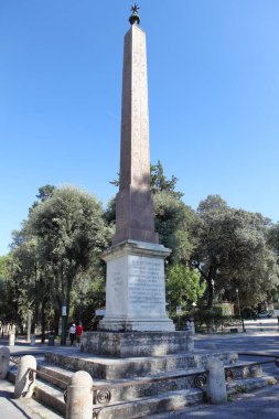 Roma, İtalya - 19 Eylül 2025: Roma, İtalya 'daki Pincian Obelisk. Beyaz mermer bir kaide üzerinde hiyeroglifler bulunan eski Mısır tarzı bir anıt, açık mavi gökyüzünün altındaki Villa Borghese bahçelerinde yer alıyor.