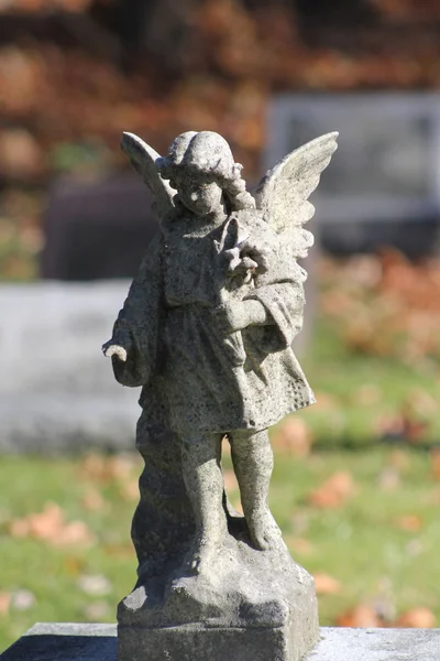 Weathered angel statue atop a cemetery headstone