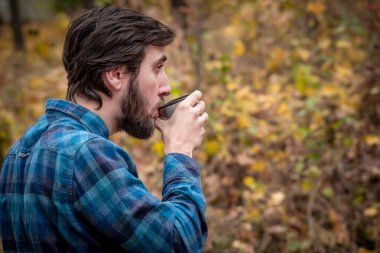 Parktaki bankta çay içen yakışıklı sakallı adam..