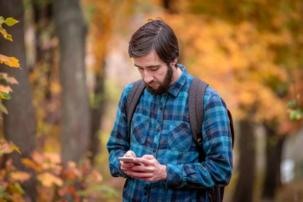 秋の公園で携帯電話を持ってる男 森の木々に囲まれて — ストック写真