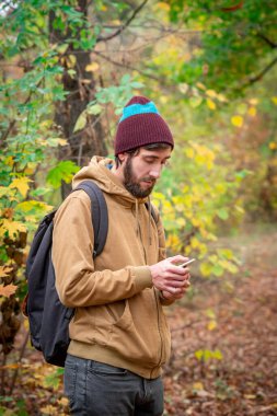 Sonbahar parkında cep telefonu olan bir adam. Ormanda ağaçlarla çevrili..