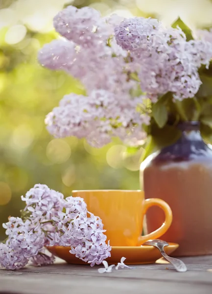 Tasse avec une cuillère et un bouquet de lilas dans un vase — Photo