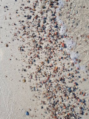 Çok renkli taşlar denizin kumlu sahilinde yatıyor.