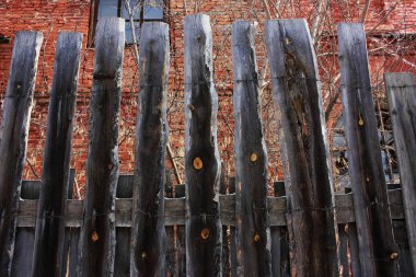 Eski ahşap bir çitin arkasındaki tuğla kırmızı bina.