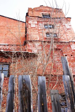 Eski ahşap bir çitin arkasındaki eski tuğla bina.