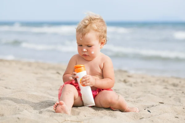 Menina adorável na praia aplicando creme protetor solar — Fotografia de Stock