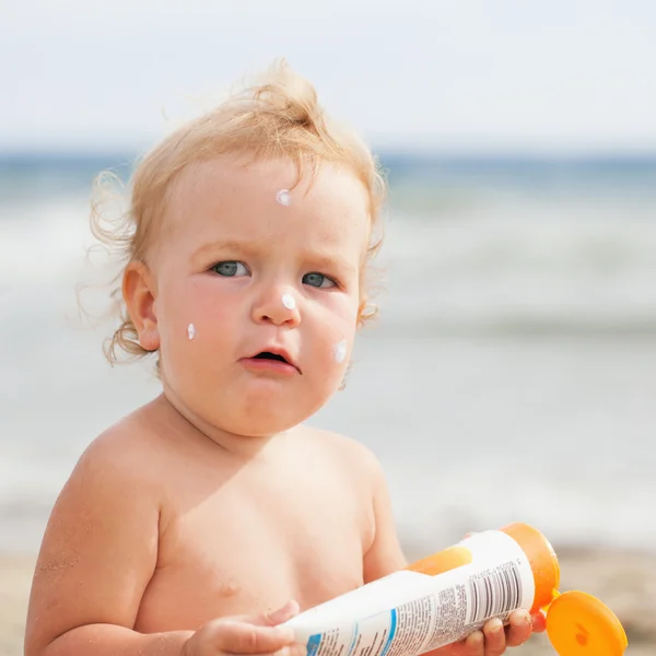 Menina adorável na praia aplicando creme protetor solar — Fotografia de Stock