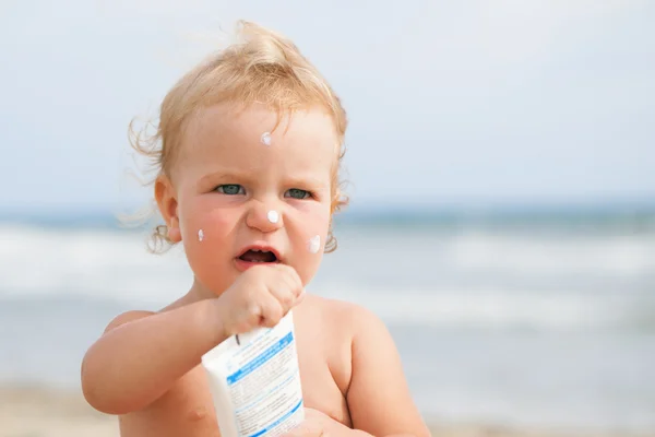 Menina adorável na praia aplicando creme protetor solar — Fotografia de Stock