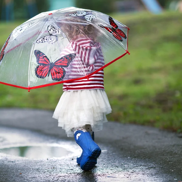 Schönes kleines Mädchen, das mit Regenschirm im Regen läuft — Stockfoto