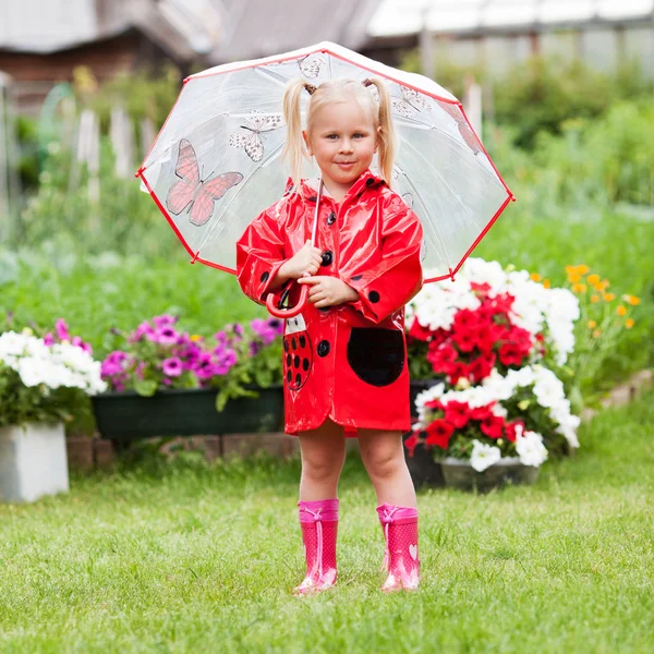 Fröhlicher Spaß hübsches kleines Mädchen in rotem Regenmantel mit Regenschirm spazieren im Park Sommer — Stockfoto