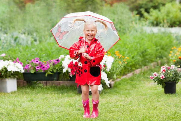 Fröhlicher Spaß hübsches kleines Mädchen in rotem Regenmantel mit Regenschirm spazieren im Park Sommer — Stockfoto
