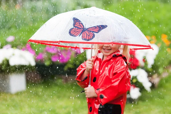 Веселой веселой маленькой девочке в красном плаще с зонтиком, гуляющей в парке летом — стоковое фото