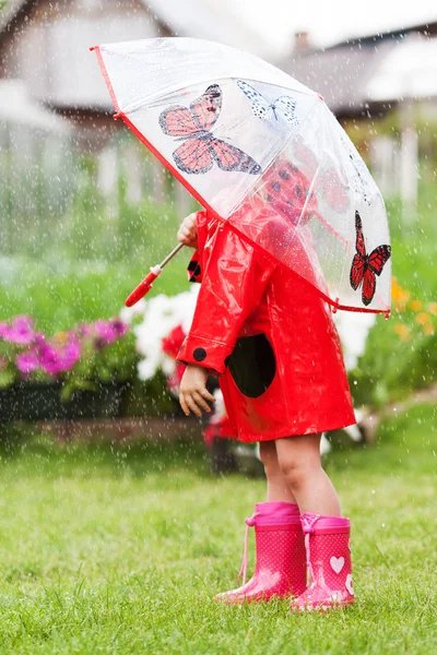 Ernsthafte nachdenkliche hübsche kleine Mädchen in rotem Regenmantel mit Regenschirm — Stockfoto