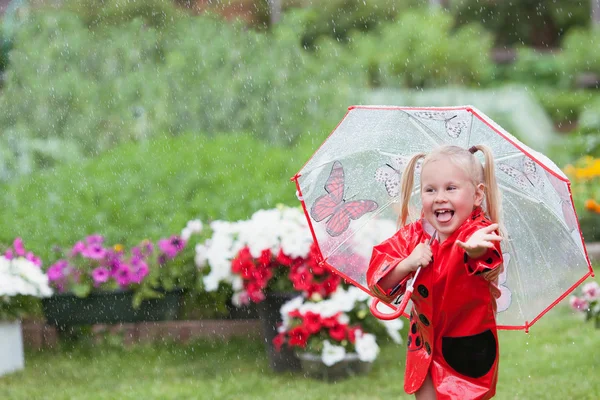 Fröhlicher Spaß hübsches kleines Mädchen in rotem Regenmantel mit Regenschirm spazieren im Park Sommer — Stockfoto