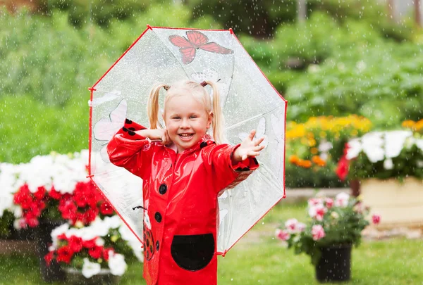 Fröhlicher Spaß hübsches kleines Mädchen in rotem Regenmantel mit Regenschirm spazieren im Park Sommer — Stockfoto