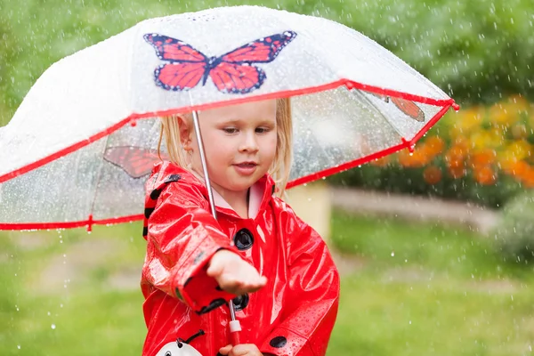 Fröhlicher Spaß hübsches kleines Mädchen in rotem Regenmantel mit Regenschirm spazieren im Park Sommer — Stockfoto
