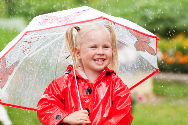 Happy fun pretty little girl in red raincoat with umbrella walking in park summer