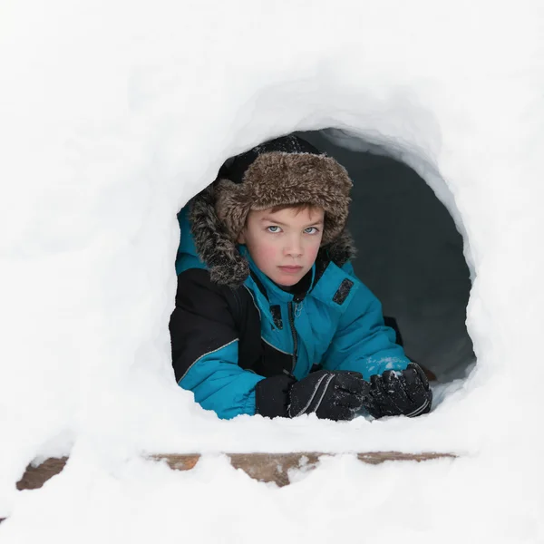 Ruddy beautiful boy in winter clothes peeking out of snow mountain, — Stock Photo, Image