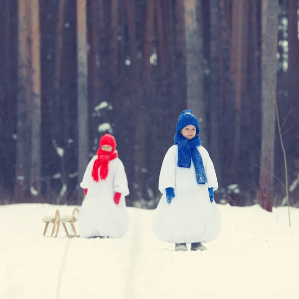 幸せな兄と妹の衣装雪だるま冬の森を歩く, — ストック写真