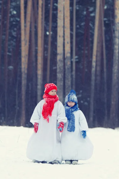 Gelukkig broer en zus in kostuums sneeuwpop wandelen in winter woud, — Stockfoto