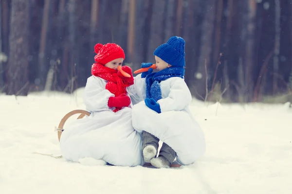 Gelukkig broer en zus in kostuums sneeuwpop wandelen in winter woud — Stockfoto