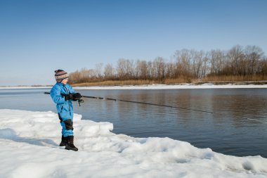 Nehri üzerinde çubuk ile kışın balık tutan çocuk.