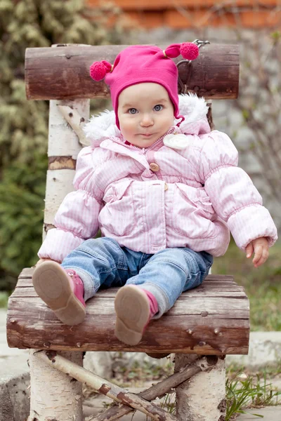 Niña en chaqueta rosa sentada en silla de madera —  Fotos de Stock