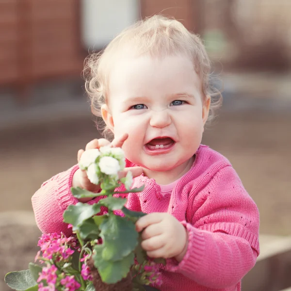 Cute baby girl in pink dress puts flowers — Stock Photo, Image