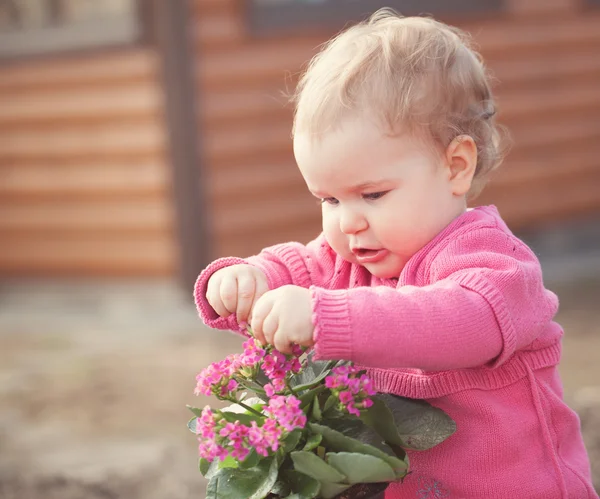 Cute baby girl in pink dress puts flowers — Stock Photo, Image